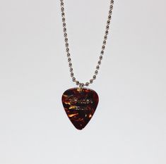 a guitar pick is hanging from a ball chain on a white surface with a silver bead necklace