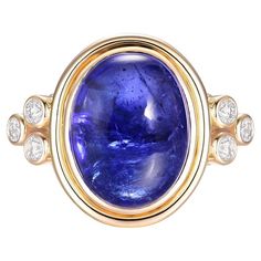 This stunning cocktail ring is a true statement piece, featuring a magnificent 11.46 carat cabochon tanzanite set in luxurious 18K yellow gold. The tanzanite's deep violet-blue hues are vivid and captivating, with the smooth, rounded cabochon cut allowing the natural beauty and color variations of the gemstone to take center stage. The tanzanite is held in a sleek bezel setting that enhances its sizable presence on the hand. Flanking the central stone on either side are trios of round brilliant- Fine Jewelry Collection, Center Stage, Round Brilliant Cut Diamond, Blue Hues, Cocktail Ring, Bezel Setting, Cocktail Rings, Round Brilliant, Ring Designs