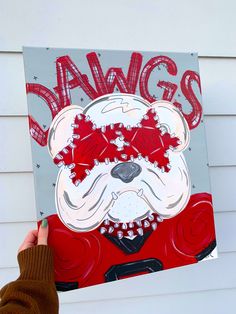 a person holding up a piece of art with the word dawgs on it