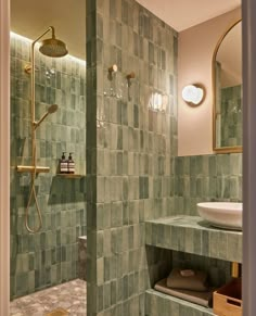 a bathroom with green tile and gold fixtures in the shower head, sink, and mirror