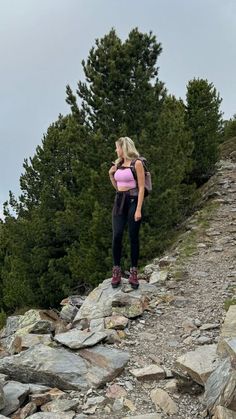 a woman with a pink backpack standing on top of a rocky hill next to trees