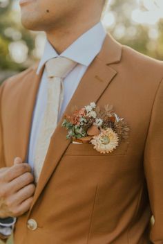 a man wearing a tan suit and flower boutonniere with his hand in his pocket