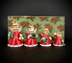 three red christmas bells with angel figurines in front of a green and red background