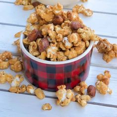 a red and black checkered bowl filled with caramel popcorn on top of a white wooden table