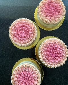 three cupcakes with pink and white frosting on them sitting on a table