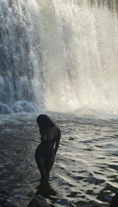 a woman standing in the water next to a waterfall