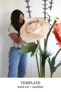 a woman standing in front of flowers with her hands on the flower stems and looking at it