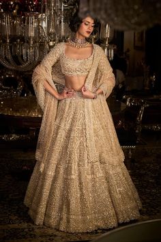 a woman in a gold lehenga standing next to a chandelier