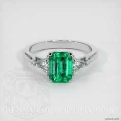 an emerald and diamond ring with three diamonds on the side, set in white gold