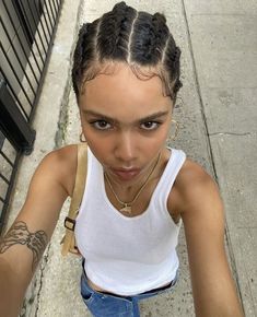 a young woman with braids on her hair is looking at the camera while leaning against a fence