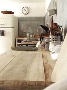 a kitchen with a wooden counter top next to a white refrigerator and clock on the wall