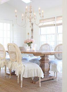 a dining room table with white chairs and a chandelier hanging from the ceiling