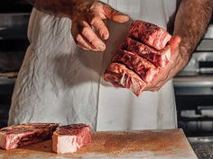 a man in an apron is holding some meat on a cutting board and another piece of meat has been cut into cubes