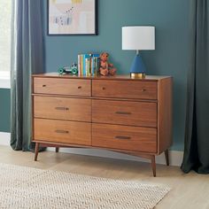 a wooden dresser with books and toys on it in a living room next to a window