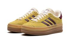 The Women’s adidas Gazelle Bold “Yellow/Burgundy” is a women’s-exclusive colorway of the retro shoe with a platform-style sole and other modifications.  The contemporary-looking adidas Gazelle Bold features a triple-stacked, raised sole.  As for the rest of the design, the shoe features a mustard yellow suede upper with burgundy leather Three Stripes on the sides.  Gold “Gazelle” branding is seen on the lateral side of the shoe.  The burgundy terry cloth heel tab matches the material used on the shoe’s inner lining.  A stacked gum rubber sole completes the look. Adidas Gazelle Platform, Gazelle Platform, Adidas Shoes Gazelle, Adidas Gazelle Bold, Gazelle Bold, Burgundy Shoes, Yellow Shoes, Stadium Goods, Retro Shoes