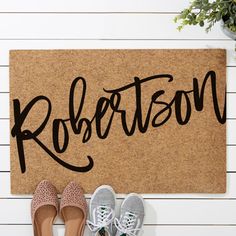 two pairs of shoes sitting on the floor next to a door mat that says robertson