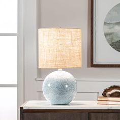 a table lamp sitting on top of a wooden dresser next to a painting and books