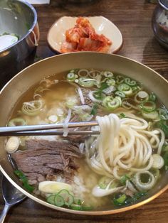 a bowl of beef noodle soup with chopsticks on the table next to it