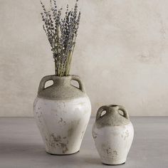 two white vases sitting next to each other on a table with lavender sprigs in them