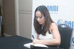 a woman sitting at a table writing on a piece of paper with a pen in her hand