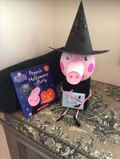 a stuffed pig wearing a witches hat next to a halloween party book on a bed