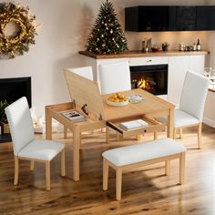 a dining room table with white chairs and a christmas tree in the fireplace behind it