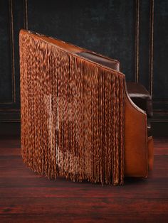 a brown leather chair with fringes on it's back and seat, in front of a black wall