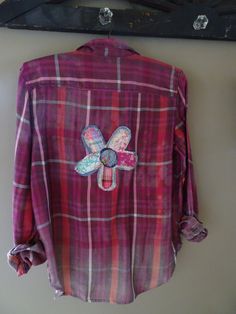 a pink plaid shirt with butterfly applique on the front and back, hanging up against a wall