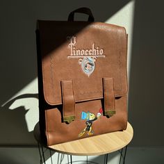 Loungefly Disney's Pinocchio Mini Satchel Backpack Is A Boxlunch Exclusive & Is Brand New But No Tags. Features Include Main Compartment, Interior Pocket, Bronze Hardware, Embroidered Jimmy Cricket, Debased Characters On The Sides, A Logo Graphic On The Front & Under The Flap Of Pinnochio's Hometown With The Stars Shining Brightly Above, Magnetic Closure Flap, Adjustable Straps. Measures 10.5 X 13.25 X 4.5" Disney Leather School Bags, Disney Leather School Backpack, Disney Leather Backpack For School, Disney Rectangular Backpack For Everyday Use, Disney Themed Rectangular Backpack For Everyday Use, Disney Backpack With Case For School, Disney Style Backpack Bag As Gift, Disney Style Backpack Bag For Gifts, Themed Backpack With Case Included