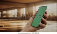 a hand holding a green cell phone in front of an empty room with large windows