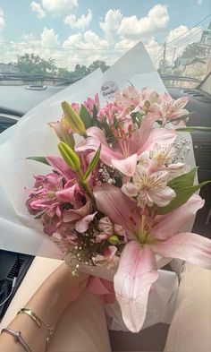 a bouquet of pink flowers sitting in the passenger seat of a car, being held by someone's hand