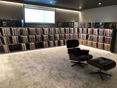 an empty chair in front of a bookcase full of cds and dvds with a large screen on the wall behind it