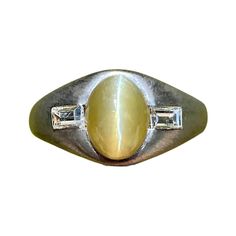 Centering an approximately ~3.00 Carat Chrysoberyl "Cats-Eye", shouldered by two Baguette-Cut Diamonds totaling 0.25 Carats, and set in PT950 Platinum (95% purity). Details: ✔ Gemstone: Chrysoberyl (Cat's Eye) ✔ Stone Cut: Cabochon (Oval) ✔ Stone Weight: 3.00 Carats ✔ Diamonds: 2 pcs Baguette-Cut Diamonds, 0.25 Carats total ✔ Diamond Cut: Baguette ✔ Diamond Weight: 0.25 Carats ✔ Ring Dimensions: 2.3 cm x 2.7 cm. ✔ Metal: PT950 Platinum (95% Purity) ✔ Era: 1980's ✔ Weight: 9.3 grams ✔ Ring Size: 7 1/4 U.S. (adjustable) Wide Band Engagement Ring, Baguette Cut Ring, Cats Eye Ring, Eye Center, Cats Eye Stone, Platinum Diamond Rings, Silver Signet Ring, Contemporary Ring, Cats Eye