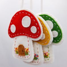 four felt mushroom ornaments hanging from strings on a white background in the shape of houses