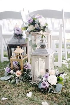 two white lanterns with flowers and greenery on the ground