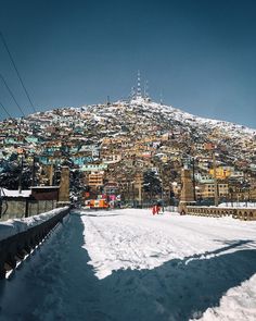 a snow covered hill with buildings on top and people walking in the snow below it