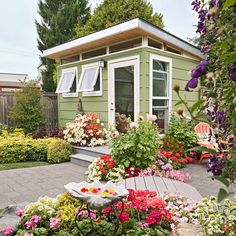 a small green house with lots of flowers around the front yard and side walk way