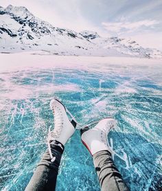 someone is standing in the water with their feet up and there are snow covered mountains behind them