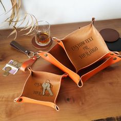 three personalized leather coasters on top of a wooden table next to a glass