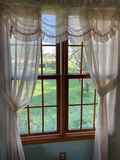 an open window with white curtains and green grass in the back ground, next to a bed