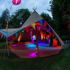 people are standing in front of a tent with colorful lights on the outside and inside