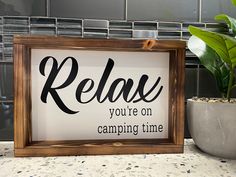 a sign that reads relax you're on camping time next to a potted plant