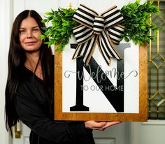 a woman holding up a sign that says welcome to our home with a bow on it