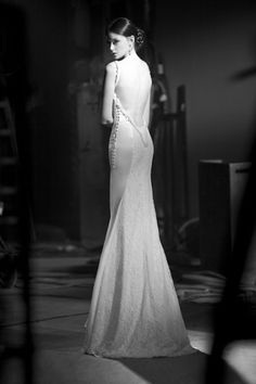 a woman in a long white dress is posing for a black and white photo with her back turned to the camera