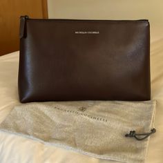 This Georgous Authentic Brunello Cucinelli Calf-Skin Super Soft Leather Clutch Bag In A Deep Rich Dark Brown Almost Has A Hint Of Maroon In Certain Lighting (Please See Pictures). It Has Gun Metal Hardware And Signature Lettering At The Front And A Leather Stitch Tag Inside With A Nylon Lining. This Beautiful Bag Is New Without Tags. It Has Never Been Carried. I Do Have The Dust Bag Which Is Also Pictured Msrp $1400 L 13” H 8” W 3.5” Elegant Satchel Pouch With Dust Bag, Elegant Soft Leather Pouch, Elegant Pouch With Leather Lining, Elegant Pouch With Leather Lining For Everyday Use, Elegant Pouch-style Business Clutch, Elegant Business Clutch In Pouch Shape, Elegant Business Clutch Shaped As A Pouch, Elegant Travel Pouch, Elegant Brown Pouch With Detachable Strap