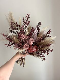 a hand holding a bouquet of flowers on a white background with red and brown leaves