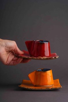 a person is holding a red cup and saucer on a plate with orange plates