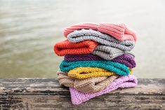 a stack of knitted scarves sitting on top of a wooden fence next to a body of water