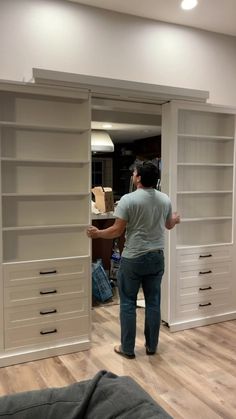 a man standing in front of a white bookcase with drawers on the bottom shelf