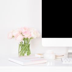 a computer monitor sitting on top of a desk next to a vase filled with flowers